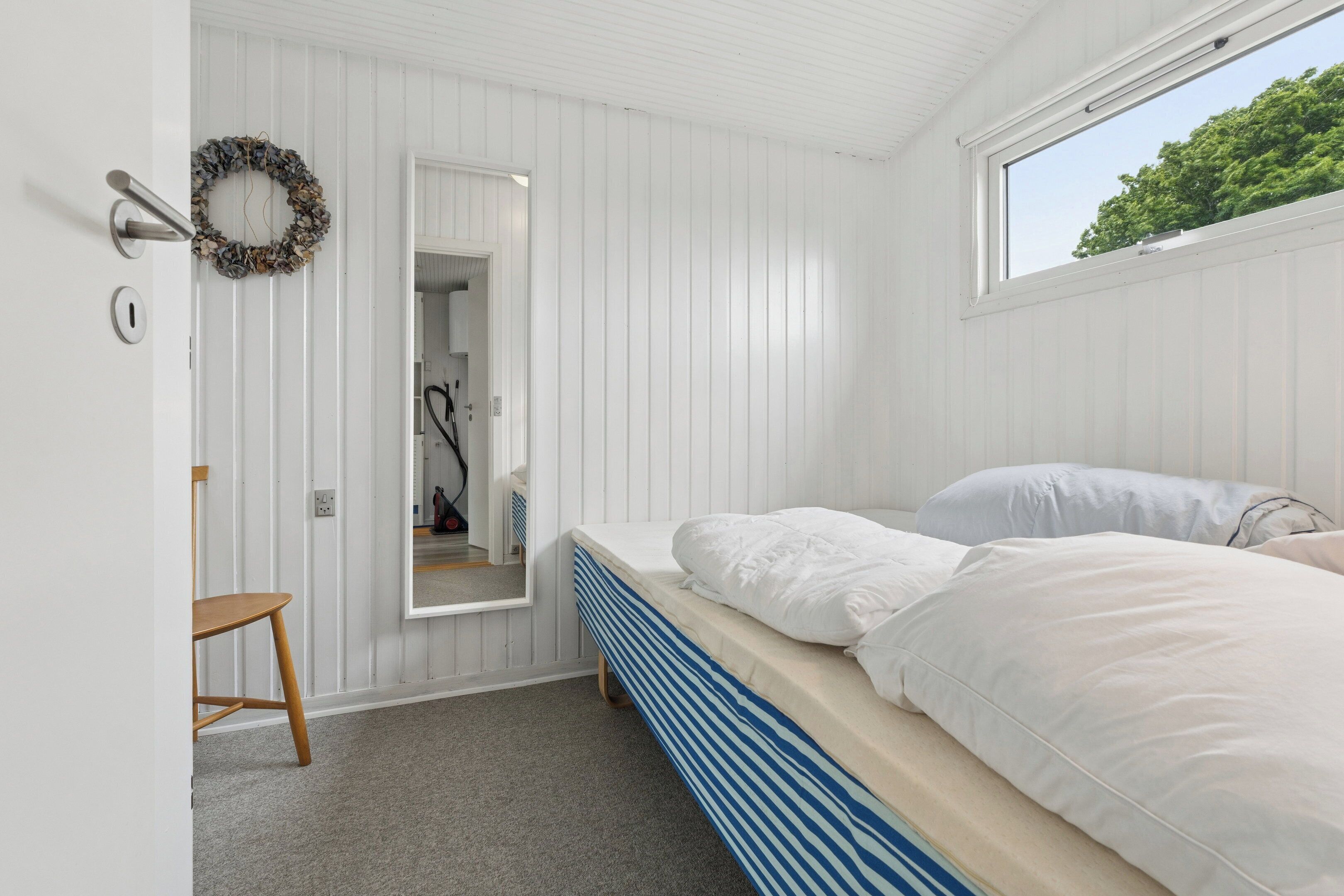 A bedroom with a bed, a chair, a mirror, and a door leading to a bathroom.