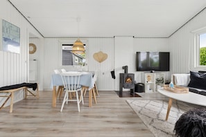 A modern living room with a dining area, a fireplace, and a television. - Nordic style summer house for two (Bogense)
