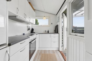 A modern kitchen with white cabinets, a built-in oven, and a window. - Nordic style summer house for two (Bogense)