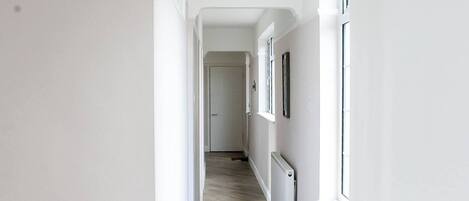 Un couloir aux murs blancs, doté d’un plancher en bois et d’un radiateur.