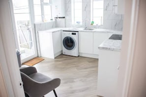 A modern kitchen with a built-in washer, white cabinetry, and a large window. - Art Deco Stylish 3 Bed Apartment (Leigh-on-Sea)