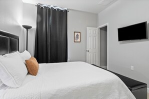 A bedroom with a bed, a bedside lamp, a TV, a door, and a framed picture on the wall. - East Austin Retreat - Pet Friendly (Austin)