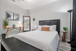 Ein modernes Schlafzimmer mit einem großen Bett, Nachttischen, einem Spiegel und einer Topfpflanze.
