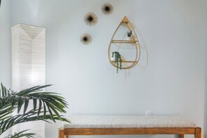 Ein Zimmer mit einer hölzernen Bank, einem an der Wand befestigten Regal mit einer Pflanze und Wanddekoration.