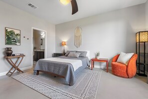 Quarto com cama, mesa de cabeceira, cadeira, abajur e um objeto decorativo na parede.