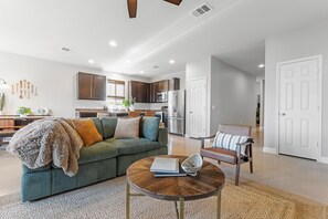 A modern living room with a green sofa, a coffee table, and a dining area with a wooden table and chairs. - East Austin Retreat - Pet Friendly (Austin)