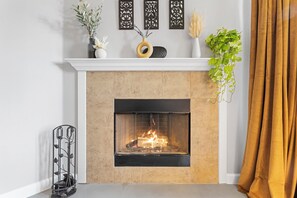 A fireplace with a fire, a white mantel, and decorative items above it. - East Austin Retreat - Pet Friendly (Austin)