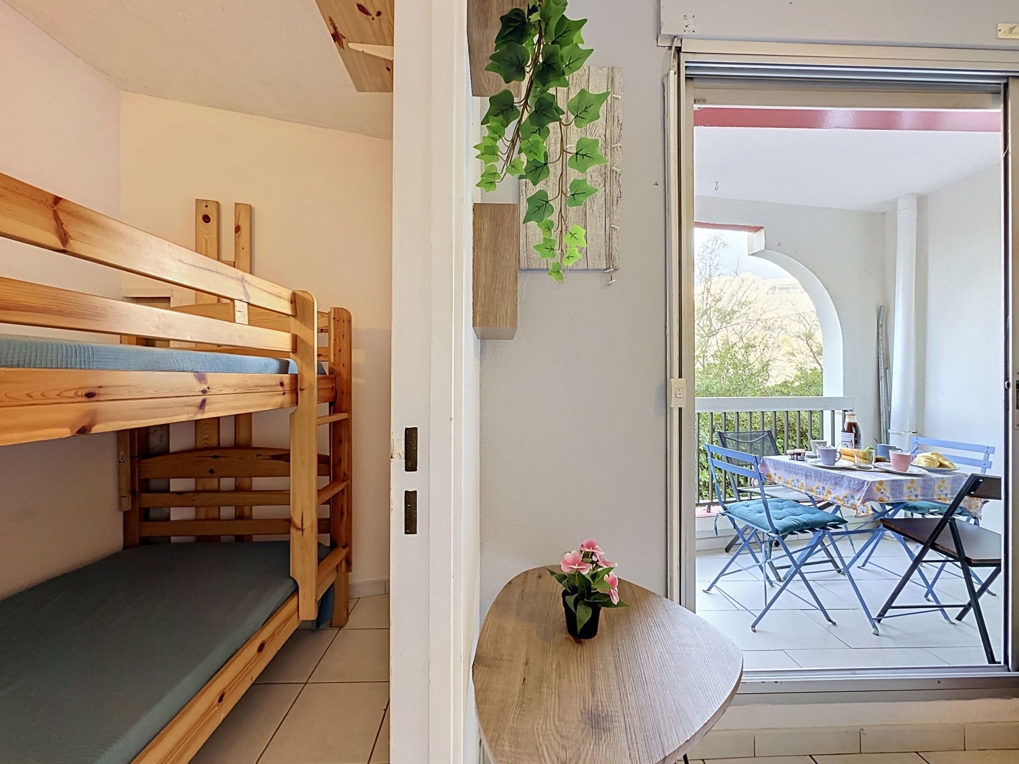 A room with a bunk bed, a small table with a potted plant, and a view of an outdoor patio area.