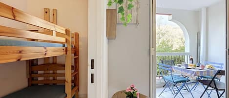 A room with a bunk bed, a small table with a potted plant, and a view of an outdoor patio area.