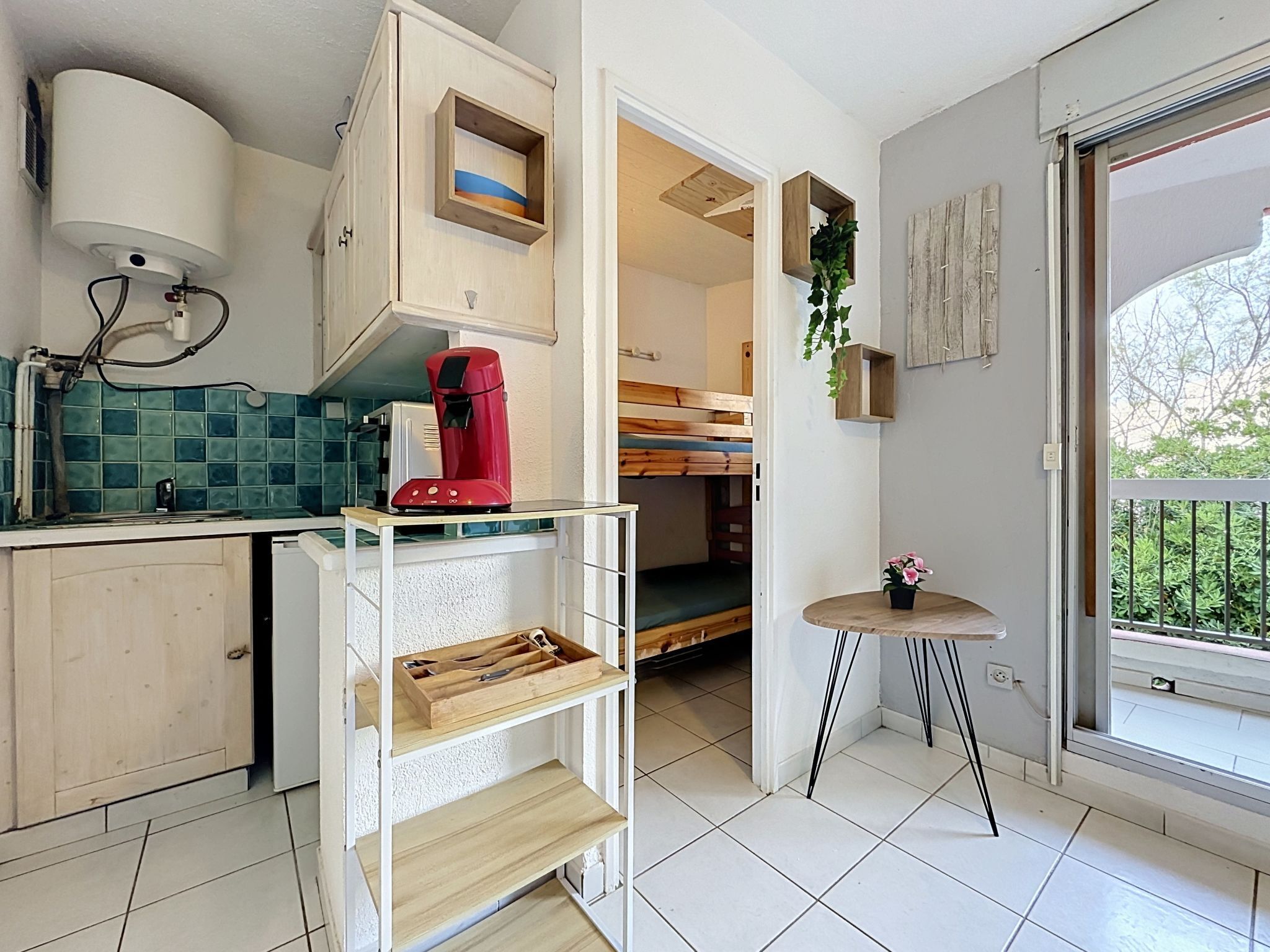 A compact kitchen with a coffee maker, a sink, and a small table with a plant.