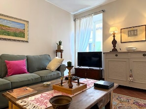 Ein Wohnzimmer mit Sofa, Couchtisch, Fernseher, Schrank und einem Gemälde an der Wand.