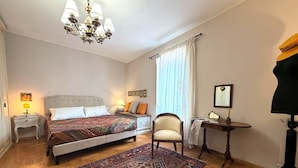 Una camera da letto con due letti, un lampadario, una sedia, una scrivania e un'ampia finestra con tende.