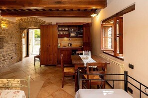 A cozy kitchen with wooden cabinets, a dining table set for four, and a stone wall. - Villa Pietrarosa: A characteristic and welcoming three-story age-old estate made of stone, with Free WI-FI. (Assisi)