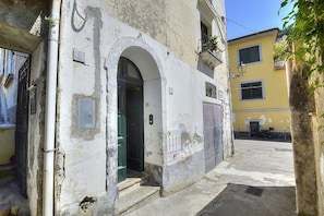 Eine enge Straße mit einem Gebäude, das einen Bogen, eine sichtbare Stromkiste und eine Schilder mit Symbolen aufweist.