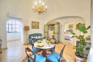 A dining area with a round table, blue upholstered chairs, a chandelier, and a view of a bedroom through an archway. - Casa Minera: An elegant independent house situated at a short distance from the beach, with Free WI-FI. (Minori)