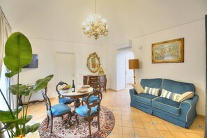 A living room with a blue sofa, a chandelier, a dining table with chairs, and a large plant. - Casa Minera: An elegant independent house situated at a short distance from the beach, with Free WI-FI. (Minori)
