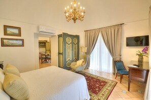 Ein Hotelzimmer mit einem großen Bett, einer Kandelaber, einem Essbereich und einem Fernseher.