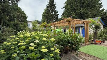 Um jardim com plantas de hortênsia, uma pérgula de madeira e uma casa com porta azul.
