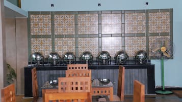 A room with a tiled wall, a long table with chairs, and a fan.