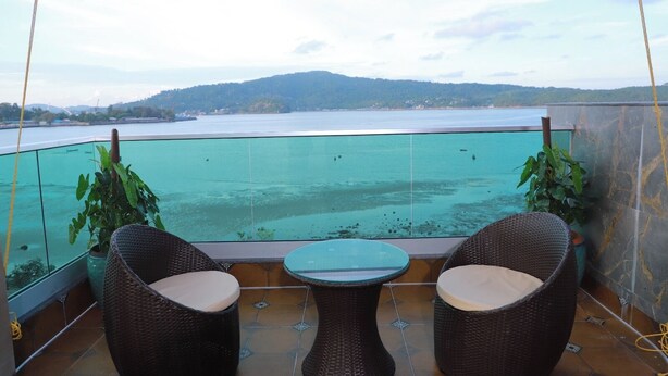 A balcony with two wicker chairs and a small table, overlooking a turquoise sea and distant hills. - Sea Deck (Port Blair)
