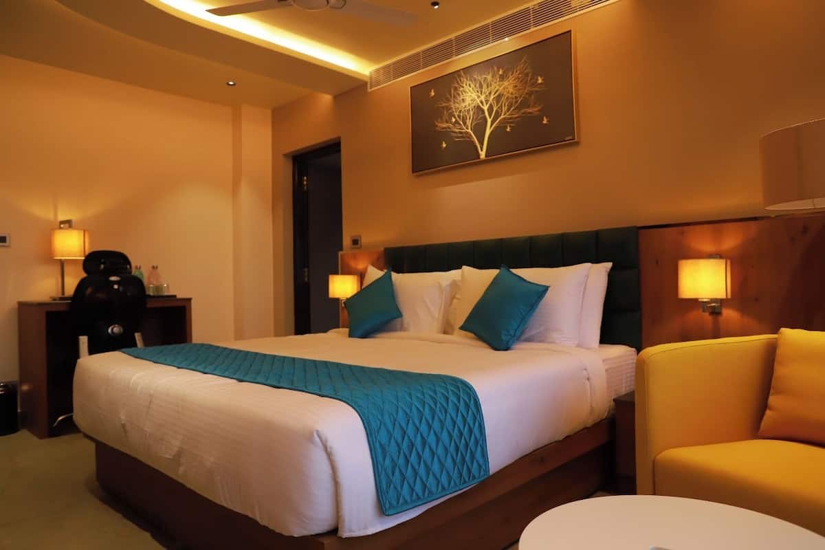 A hotel room with a bed, bedside tables, a chair, a desk, and a wall-mounted artwork.