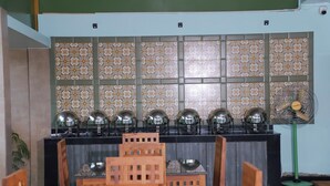 A dining area with a long table, chairs, a buffet with food warmers, and a wall with patterned tiles. - Sea Deck (Port Blair)