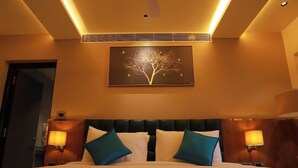 A hotel room with a bed, two wall-mounted lamps, a ceiling fan, and a painting of a tree. - Sea Deck (Port Blair)