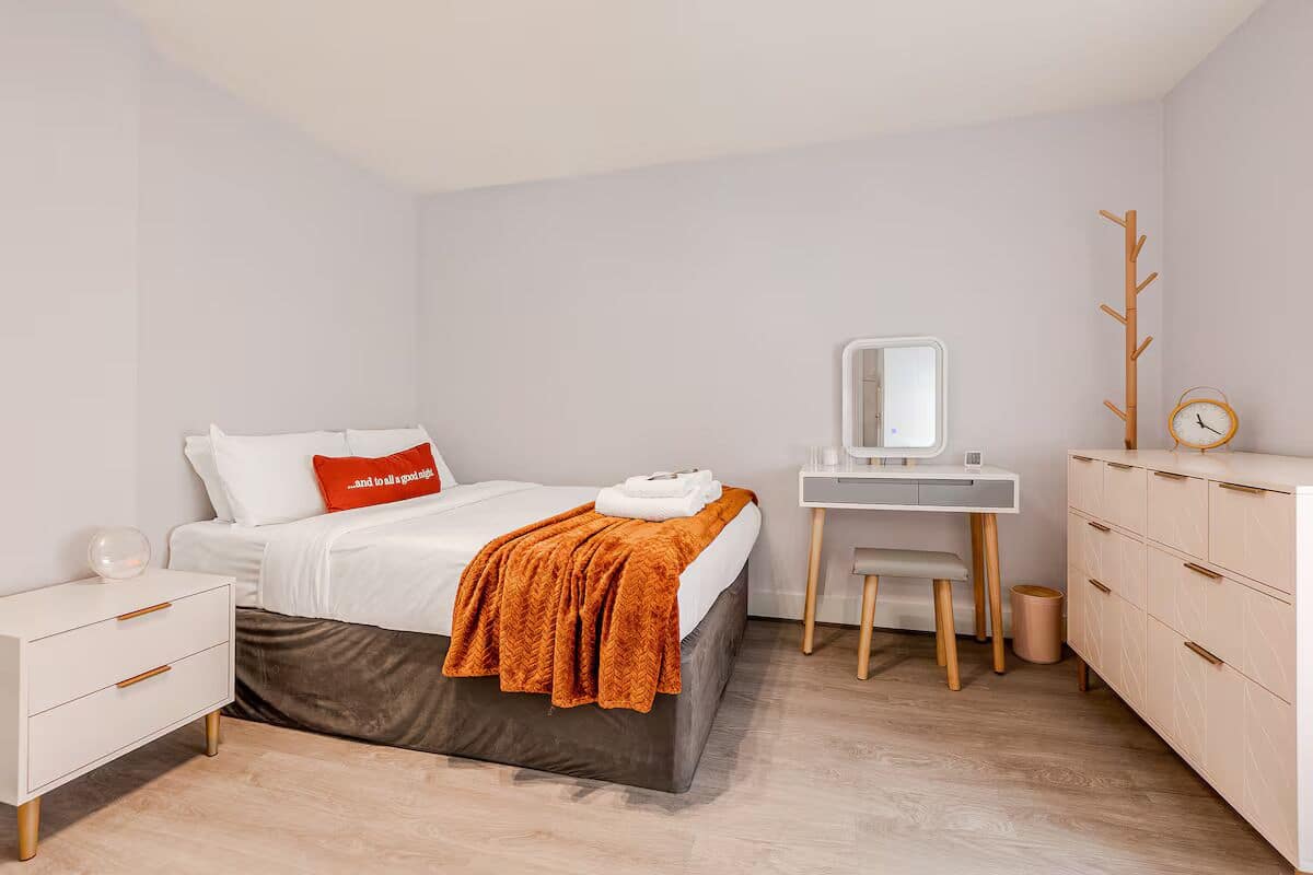 A bedroom with a bed, a desk, a dresser, a mirror, and a coat rack.