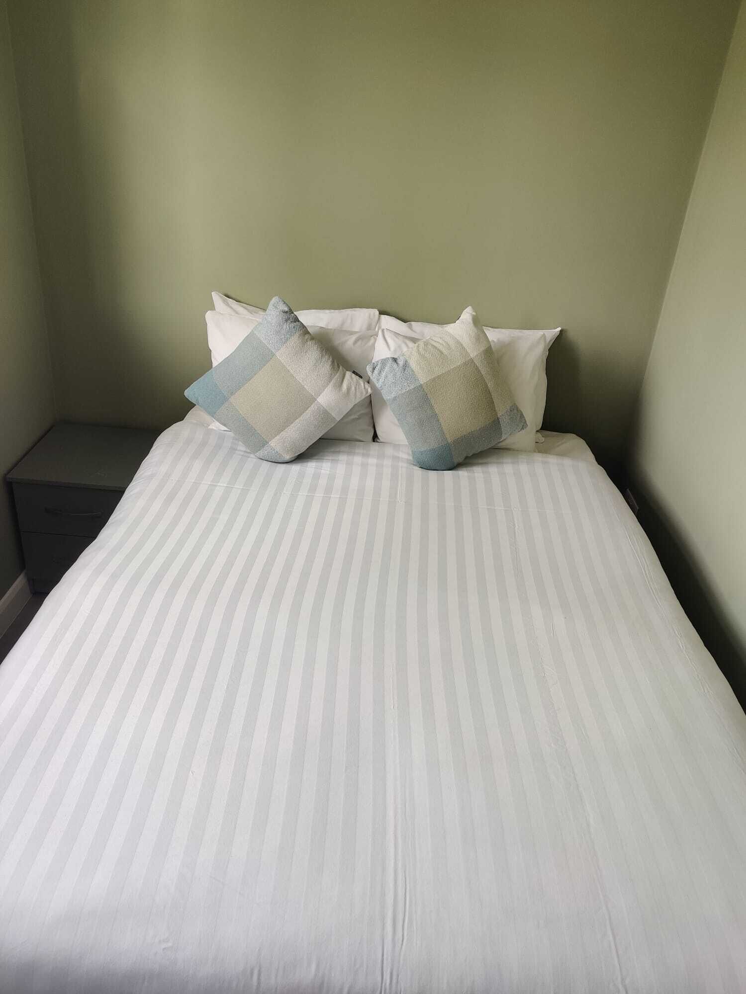 Una cama con ropa de cama a rayas y dos almohadas de estampado cuadriculado.
