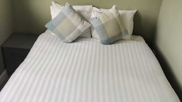 Una cama con ropa de cama a rayas y dos almohadas de estampado cuadriculado.
