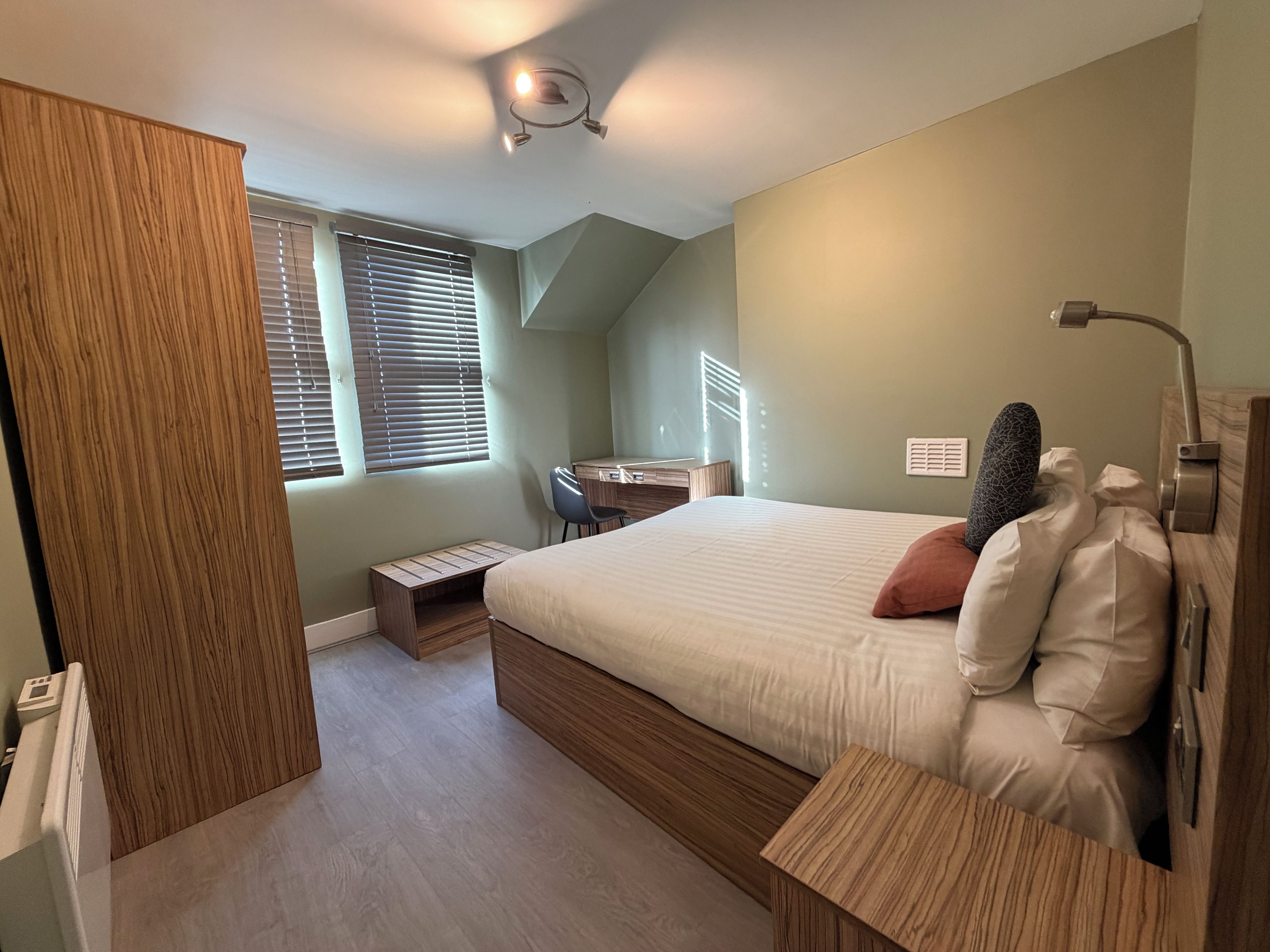 A bedroom with a bed, bedside table, and a desk with a chair.