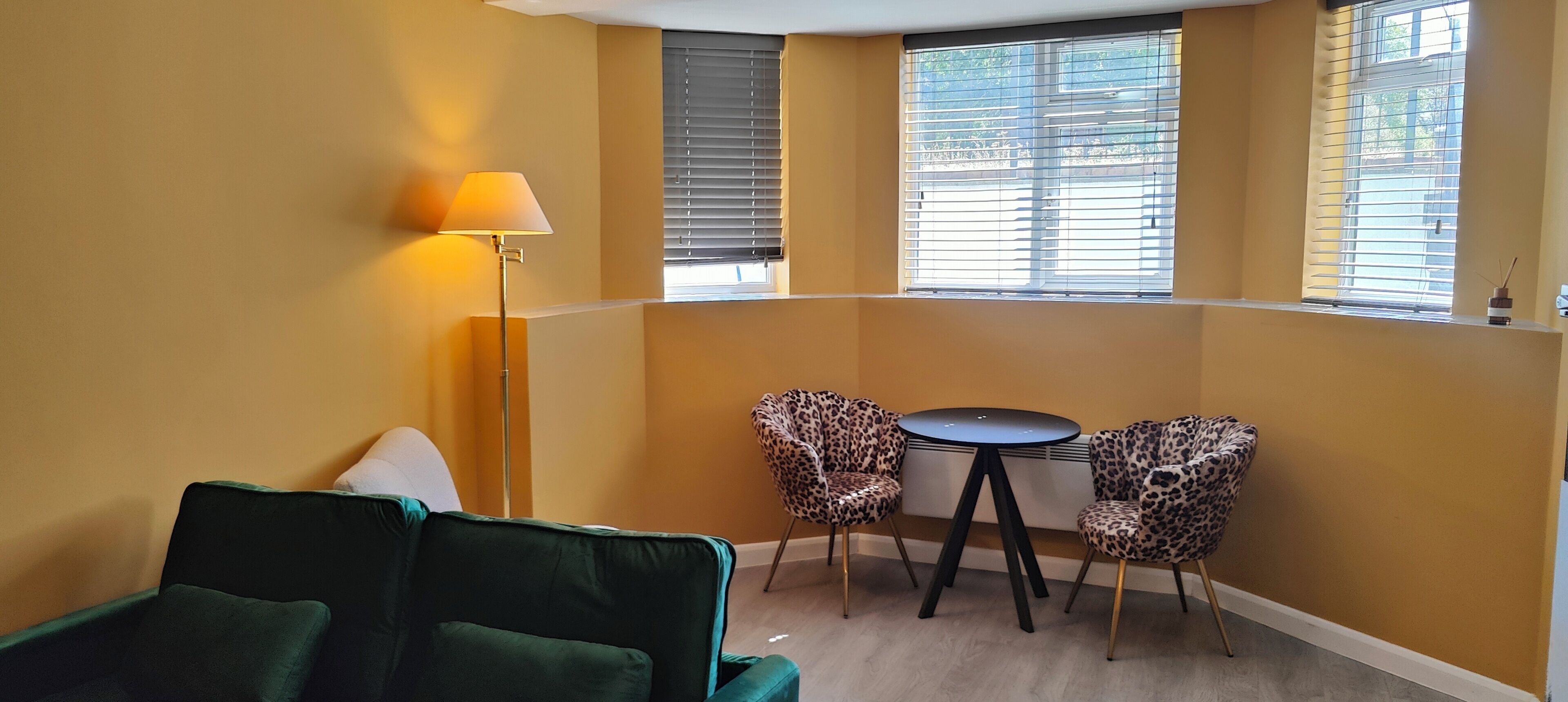 A corner room with a green sofa, two leopard print chairs, a small round table, and a floor lamp.