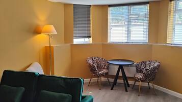 A corner room with a green sofa, two leopard print chairs, a small round table, and a floor lamp.