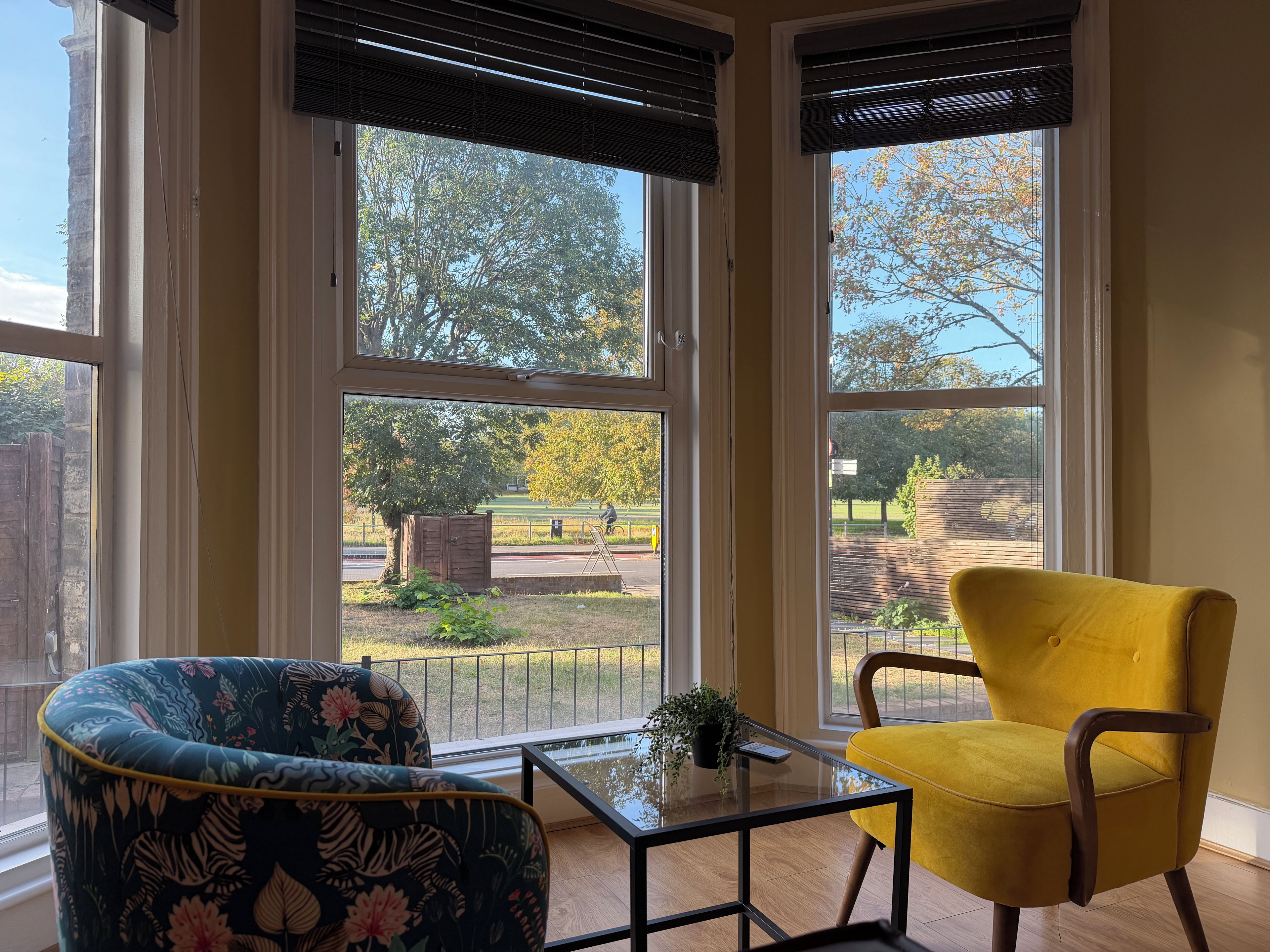 A room with large windows, a glass table, a floral armchair, and a yellow chair.