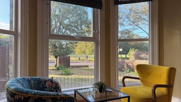 A room with large windows, a glass table, a floral armchair, and a yellow chair.