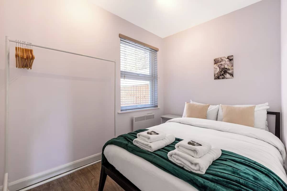 A bedroom with a bed, a window with blinds, a radiator, and a towel rack.