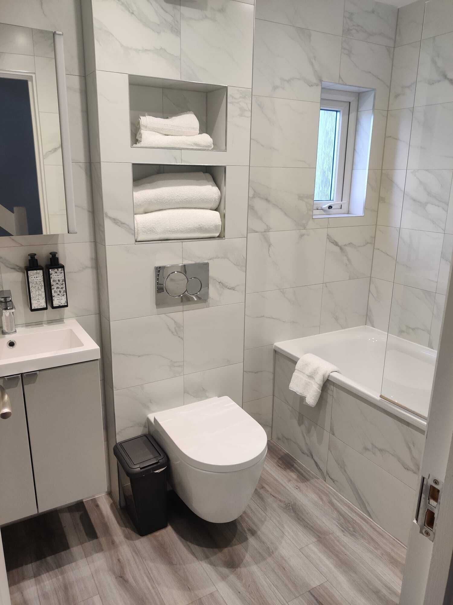 Un baño moderno con inodoro, lavamanos y estantes empotrados para toallas.