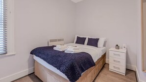 A bedroom with a bed, bedside table, and a window with blinds. - Samko Suites Clapham (London)