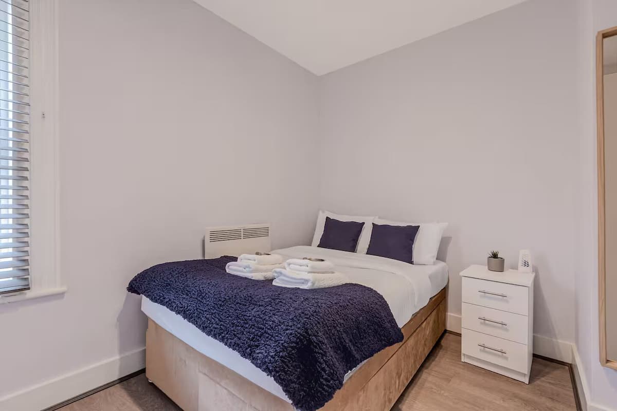 A bedroom with a bed, bedside table, and a window with blinds.
