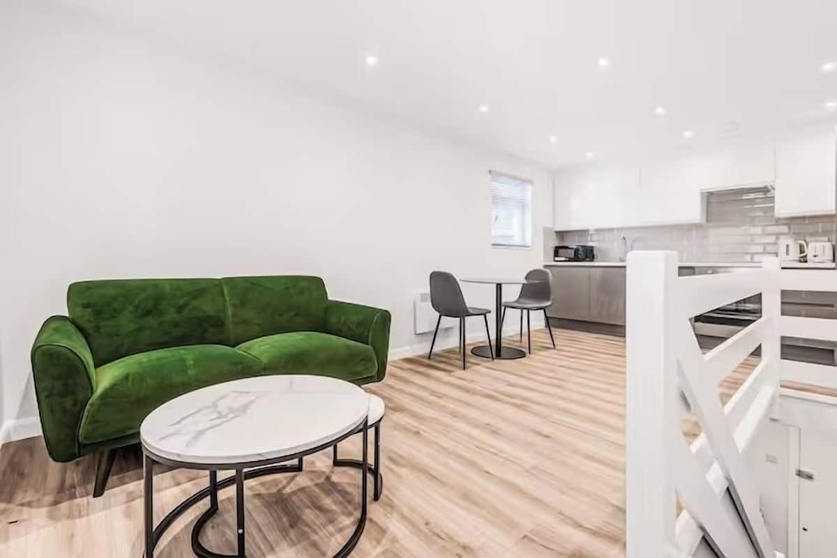 A modern living area with a green sofa, a round table, and a kitchen in the background.