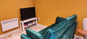 Una sala de estar con un sofá color turquesa, un mueble blanco para centro de entretenimiento con televisor de pantalla plana y un radiador blanco.