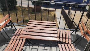 Un balcón con barandilla de metal, bancos de madera y vista a una carretera con un camión azul.