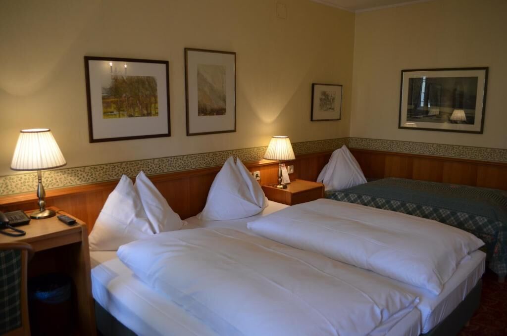 Habitación de hotel con dos camas, lámparas de noche, un escritorio con teléfono y cuadros en las paredes.