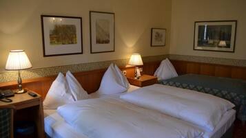 Habitación de hotel con dos camas, lámparas de noche, un escritorio con teléfono y cuadros en las paredes.
