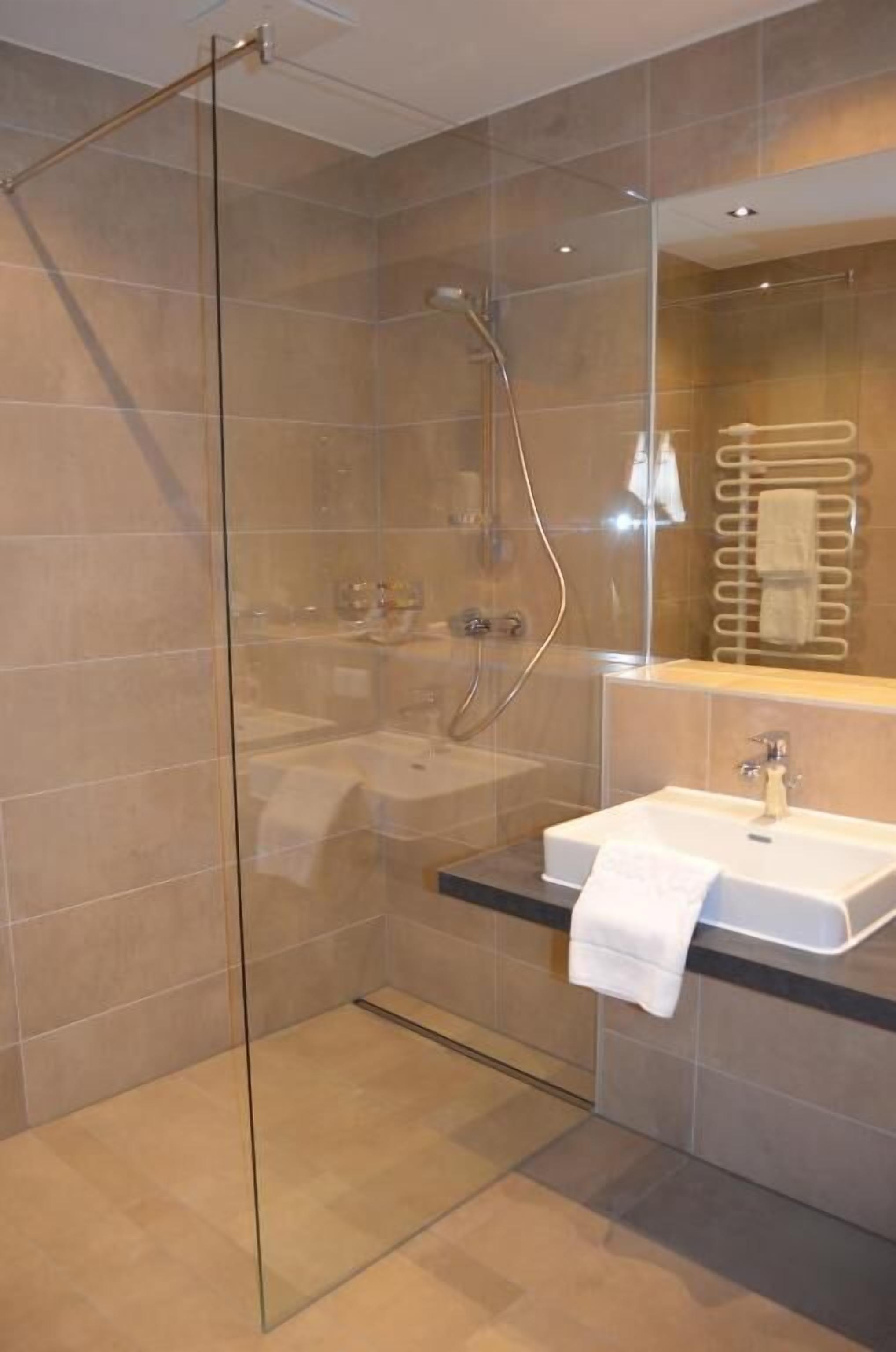 Un baño moderno con ducha de vidrio, un lavabo con una toalla y un espejo sobre el lavabo.