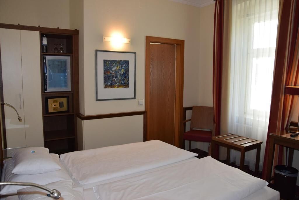 Een hotelkamer met een bed, een stoel, een bureau, een schilderij aan de muur en een garderobe.