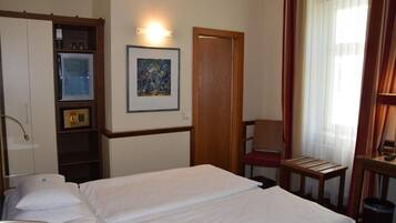 Een hotelkamer met een bed, een stoel, een bureau, een schilderij aan de muur en een garderobe.