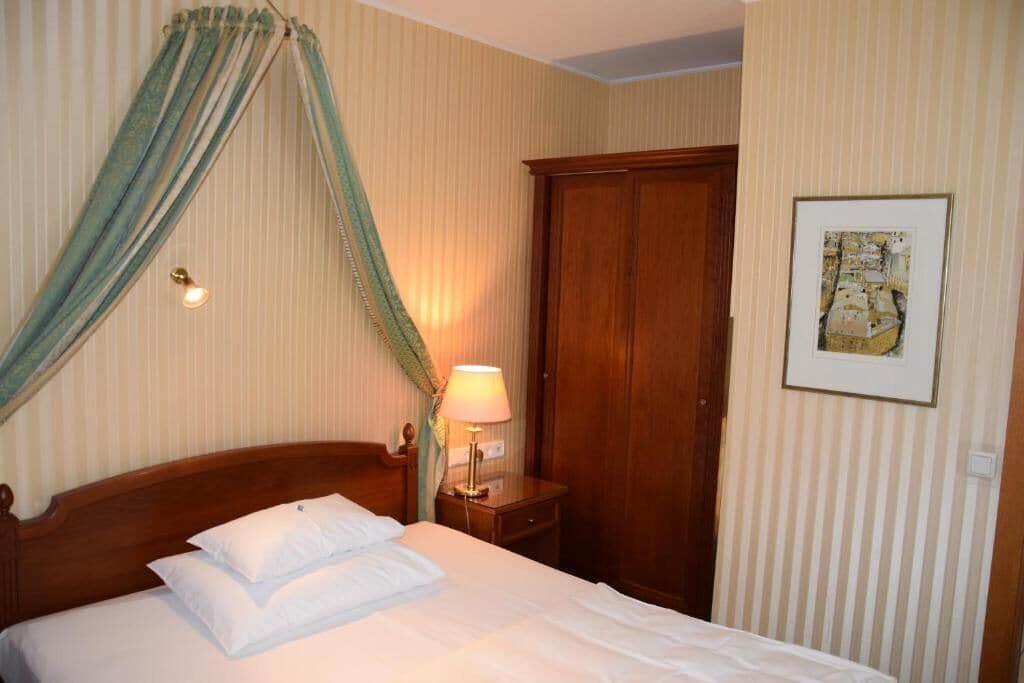 Una camera d'albergo con un letto, un comodino con una lampada, un armadio e un quadro appeso al muro.