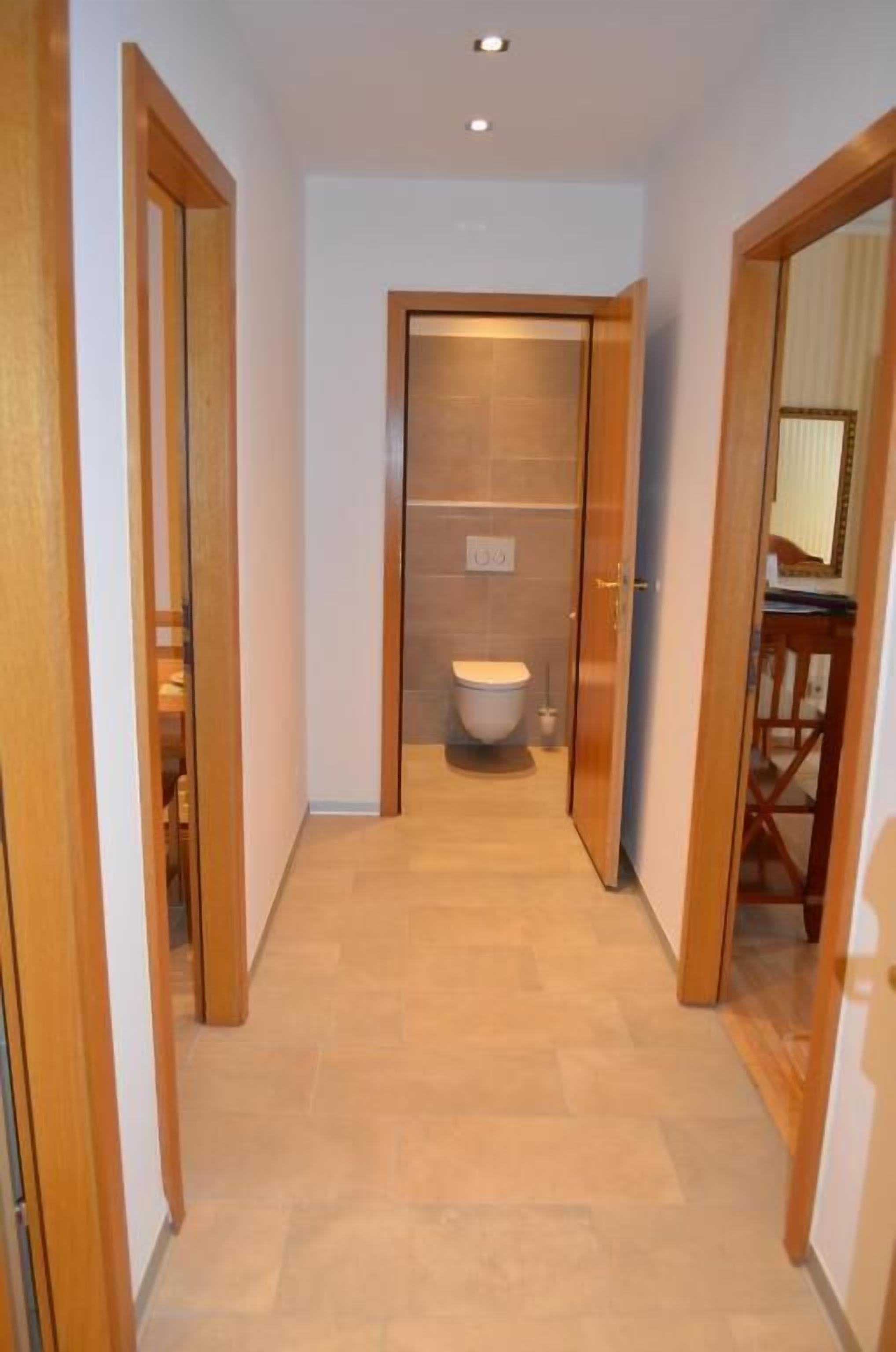 Ein schmaler Korridor mit Holztüren an beiden Seiten, der zu einem Badezimmer mit Toilette und Spiegel führt.
