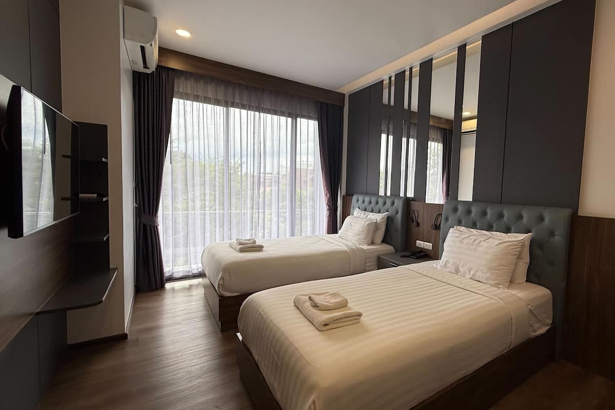 A hotel room with two beds, a TV, and a large window with curtains.